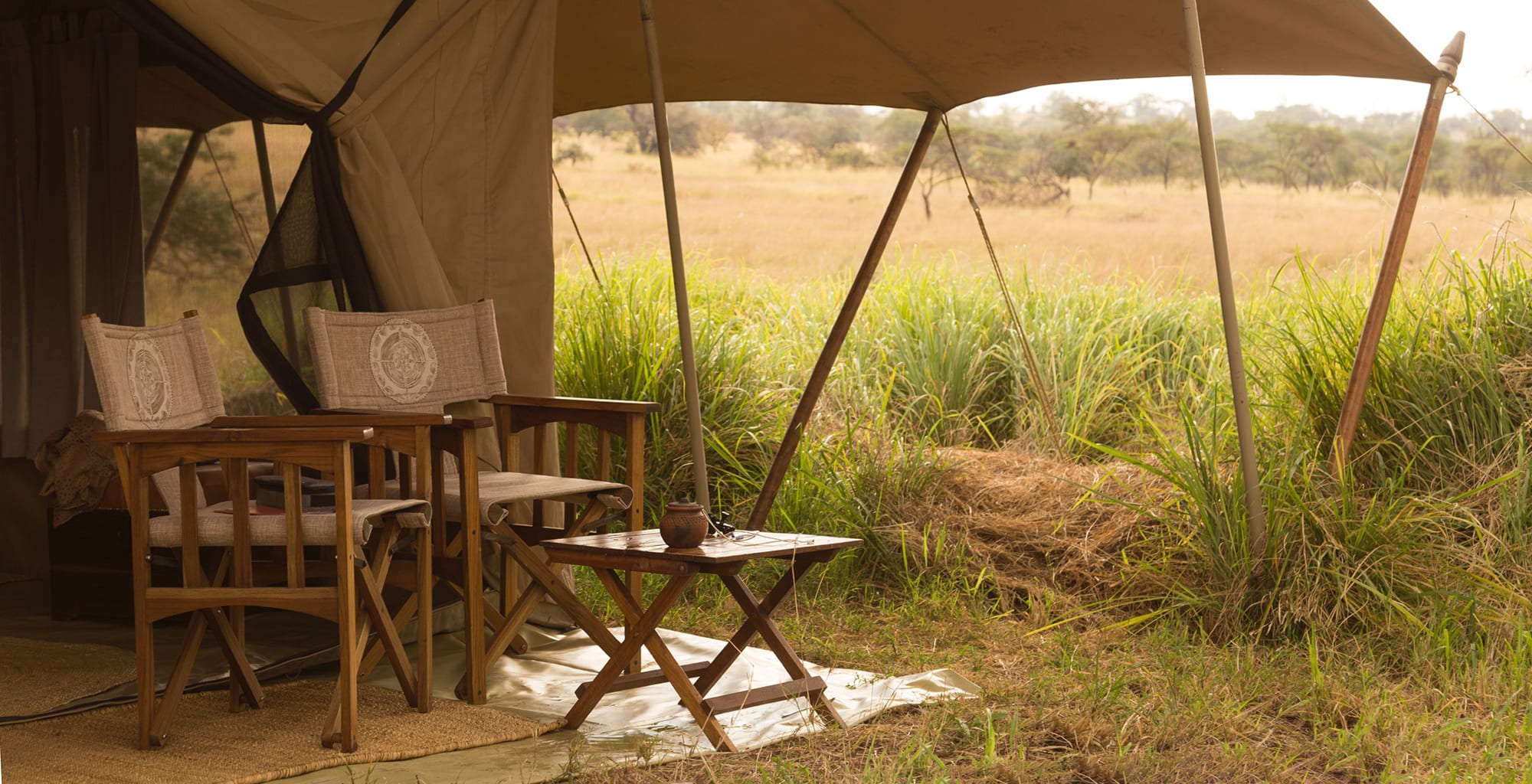 Wooden campaign chairs and a side table outside a luxury safari tent in Tanzania