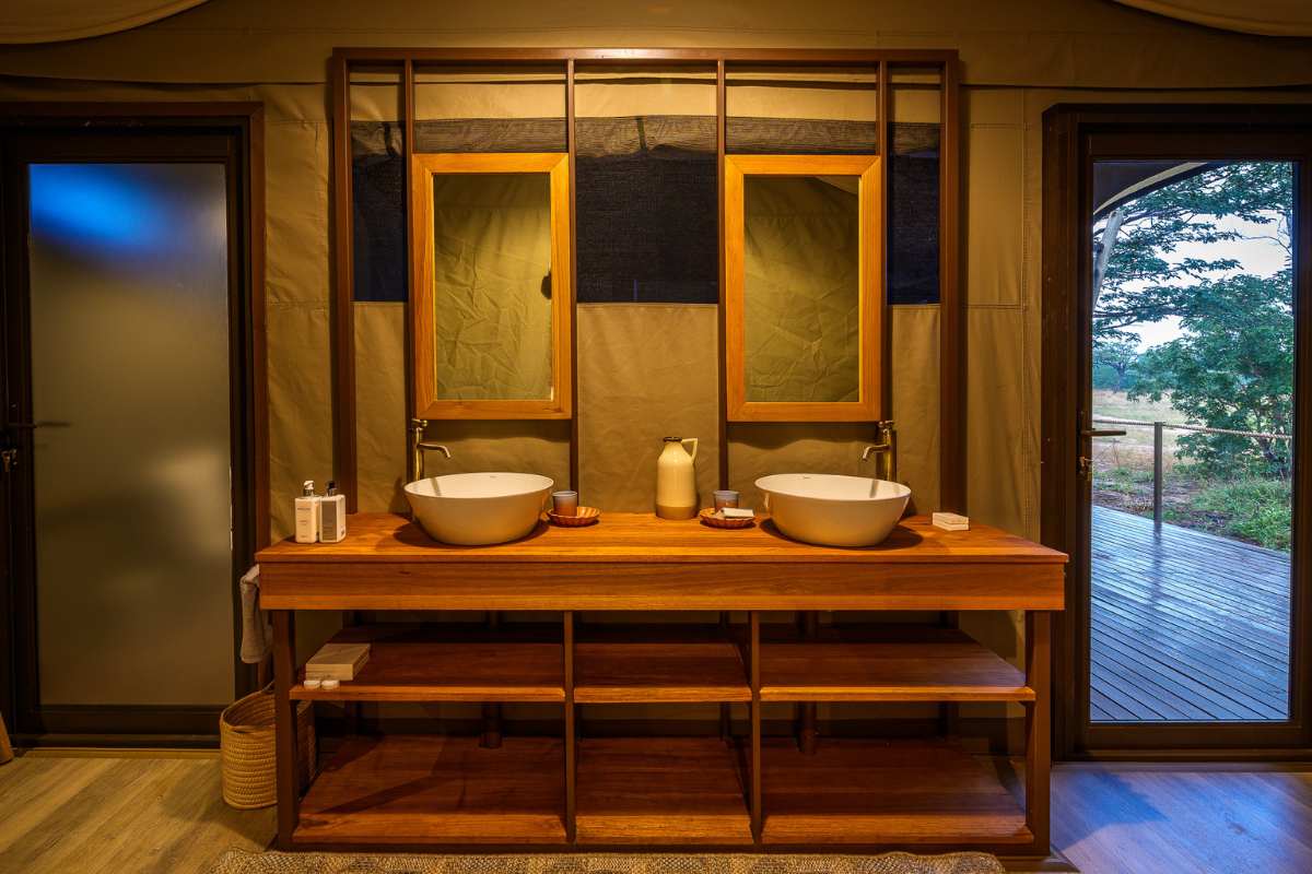 Tented camp bathroom with a custom timber double vanity, vessel sinks and framed mirrors against canvas walls